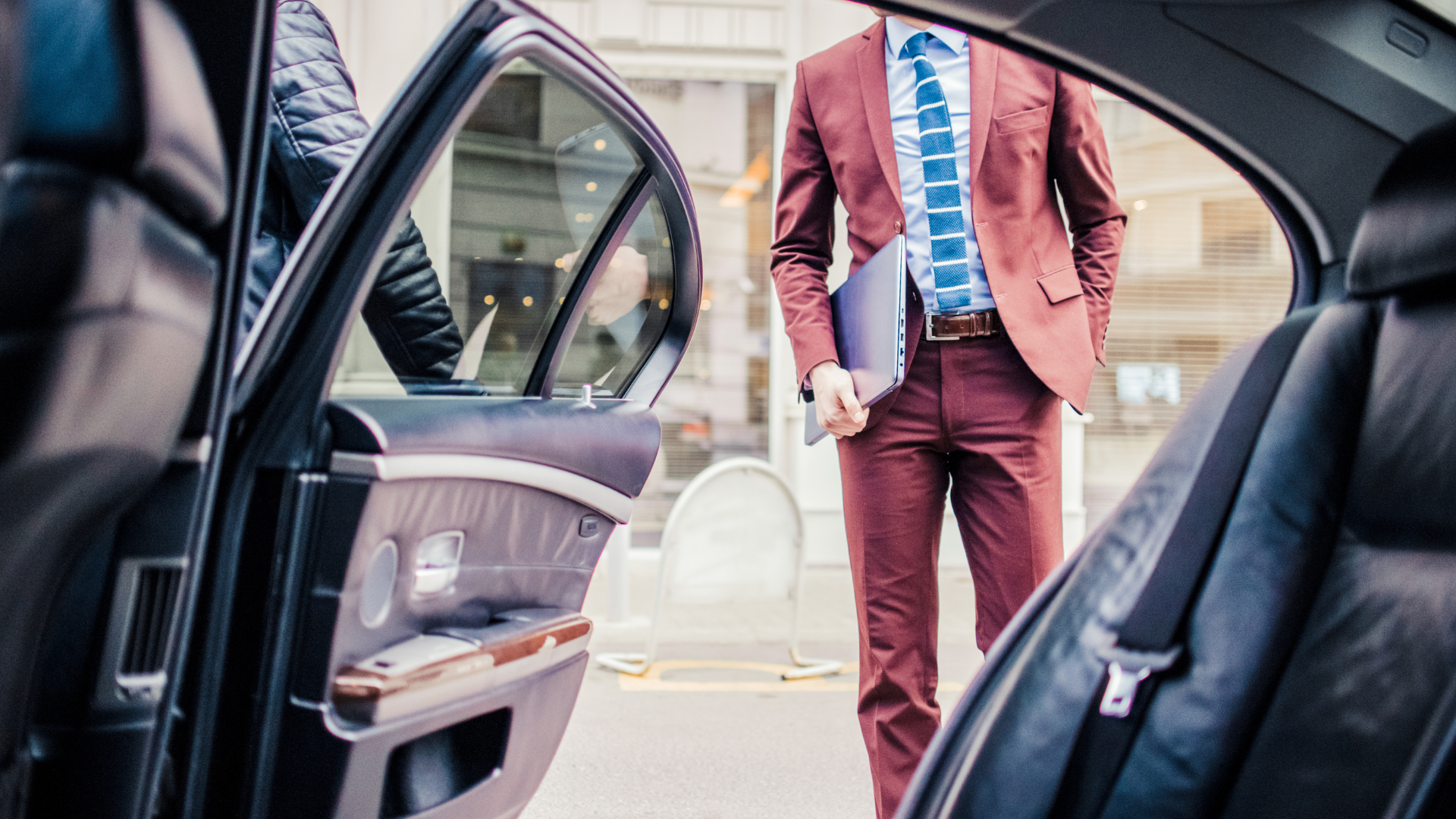 Executive in a tailored suit walking to the open rear door of a chauffeured car, folder in hand